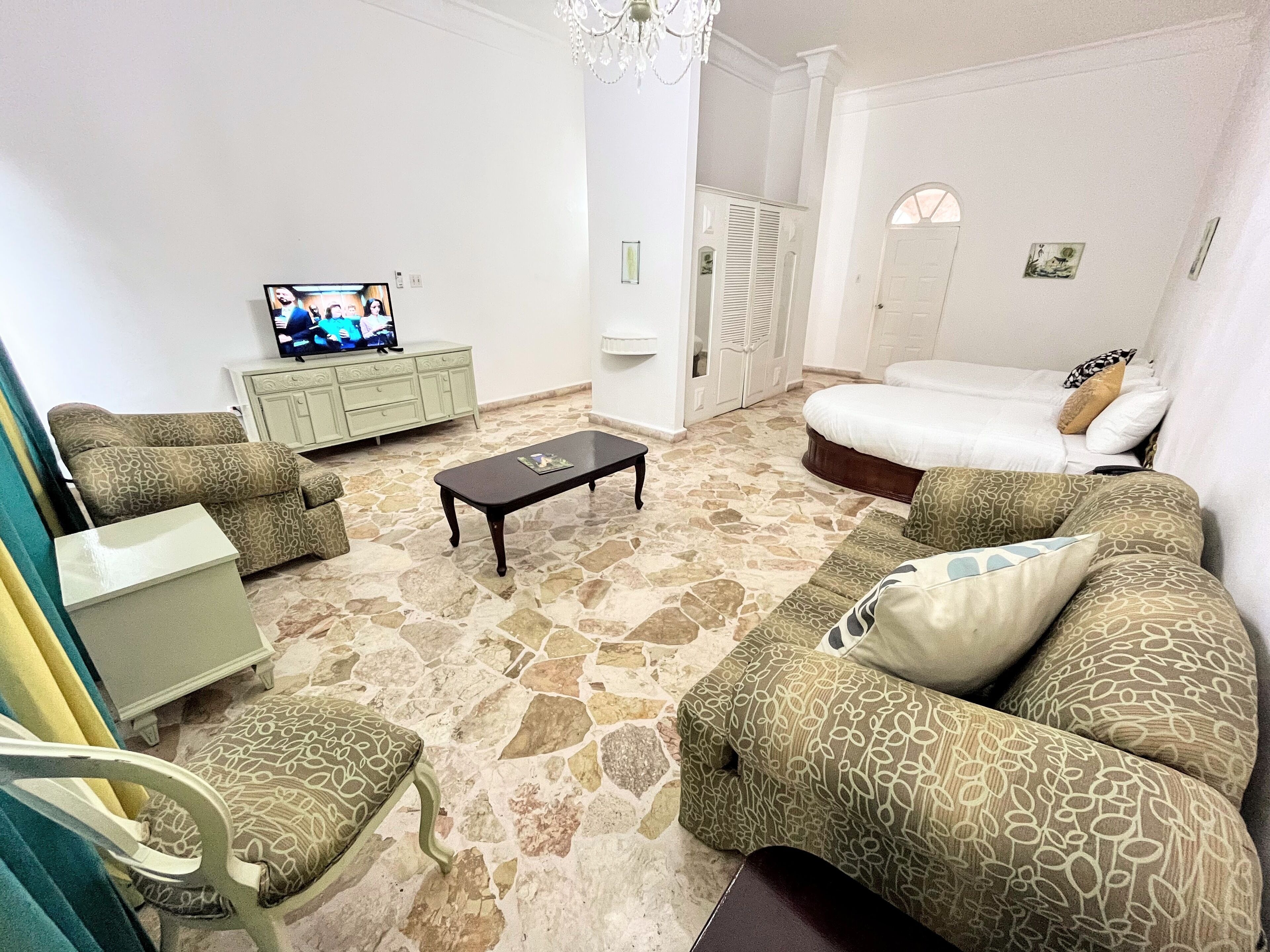 Una sala de estar con sofá, sillón, mesa de centro, televisor y cama.