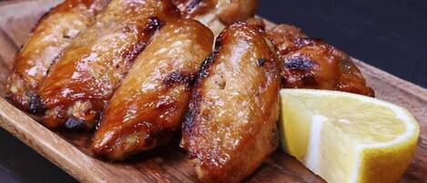 A wooden serving board with grilled chicken wings and a slice of lemon.
