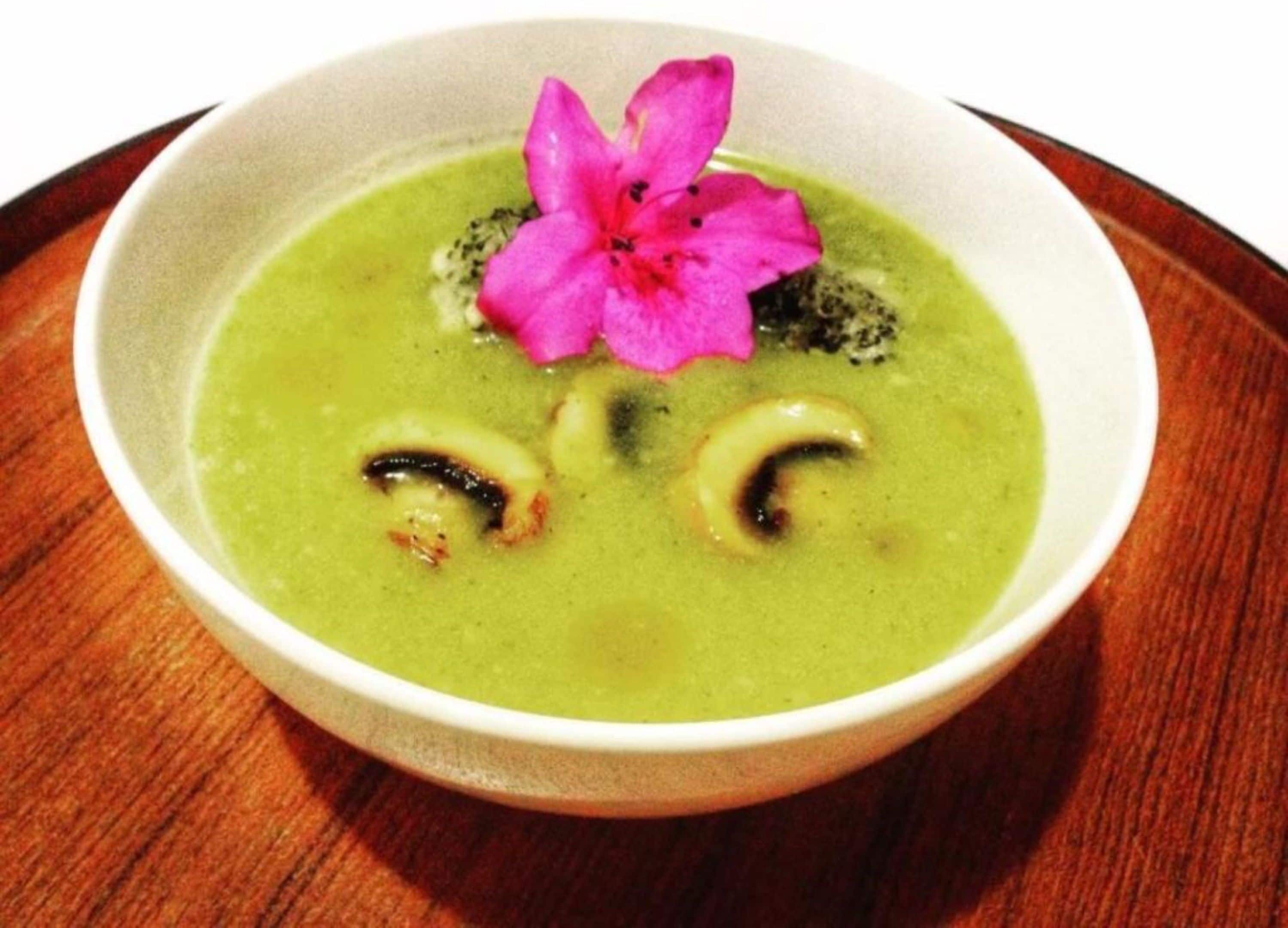 Un bol de soupe verte, décoré d’une fleur rose, est posé sur une table en bois.