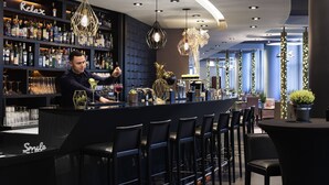 Zona de bar con un cantinero, estanterías llenas de botellas de licor e iluminación moderna.