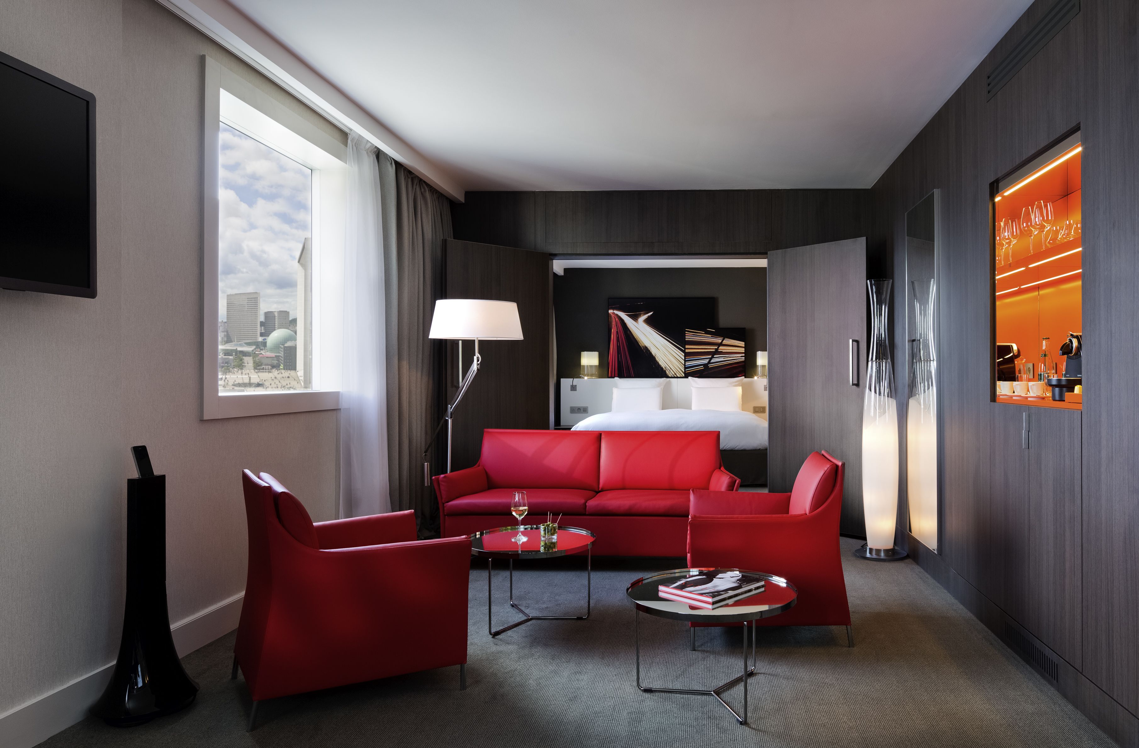 A hotel room with a red sofa, a small coffee table, a TV, and a bed.