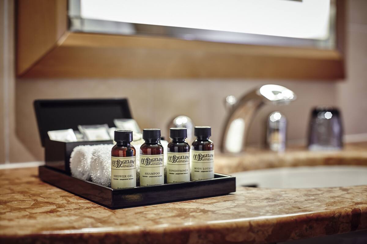 A tray with four bottles of Bigelow body lotion and a white towel on a marble countertop.