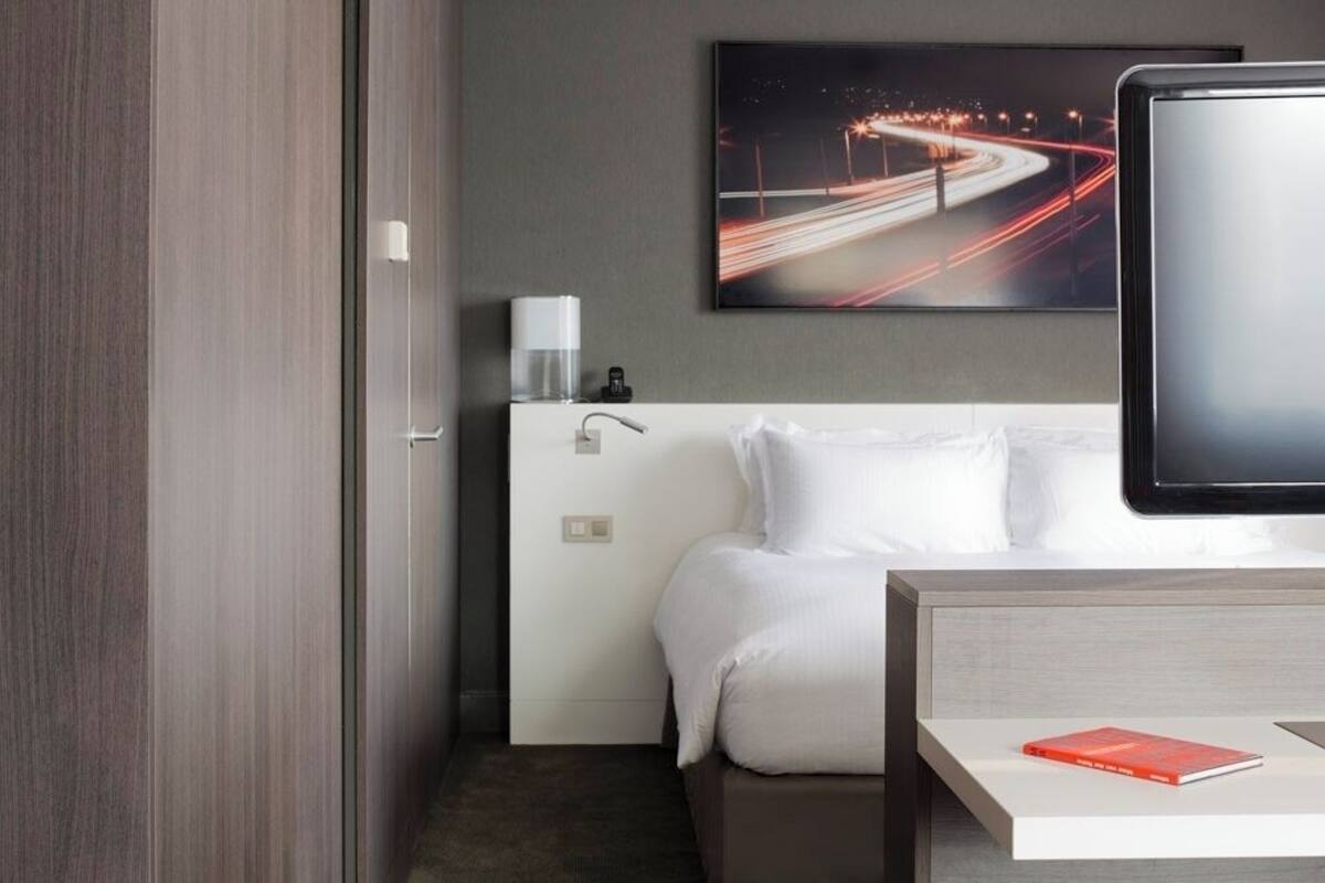 A hotel room with a bed, bedside table, and a wall-mounted TV.