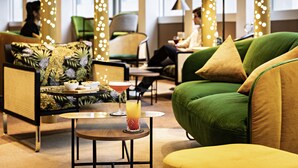 Un área de descanso moderna con sofás verdes, una mesa redonda con una bebida y luces colgantes.