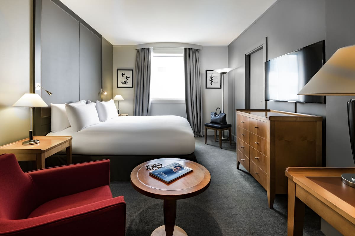 A hotel room with a bed, a desk, a chair, a TV, and a dresser.