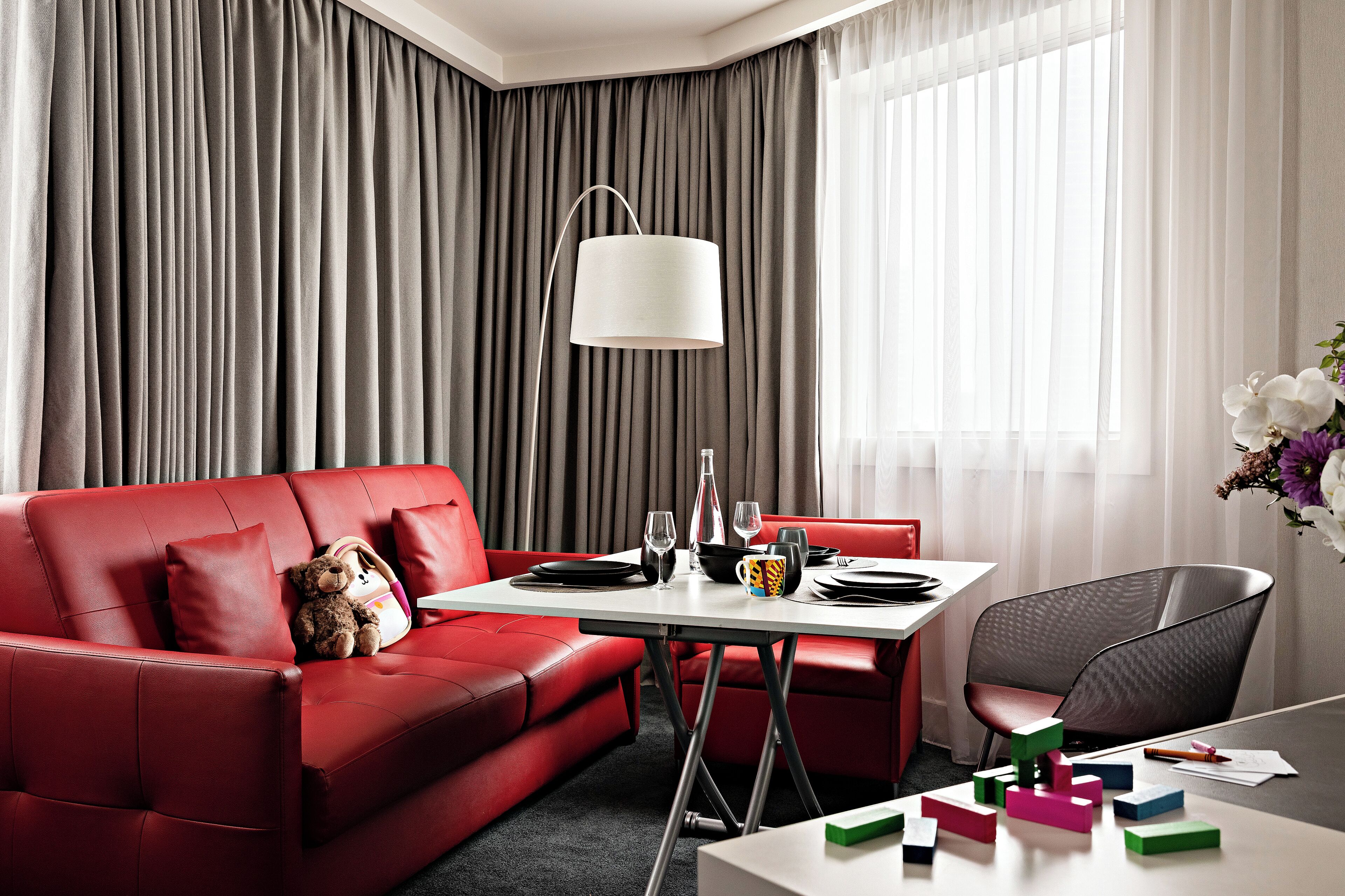 A modern hotel room with a red leather sofa, a white table, and a black chair.