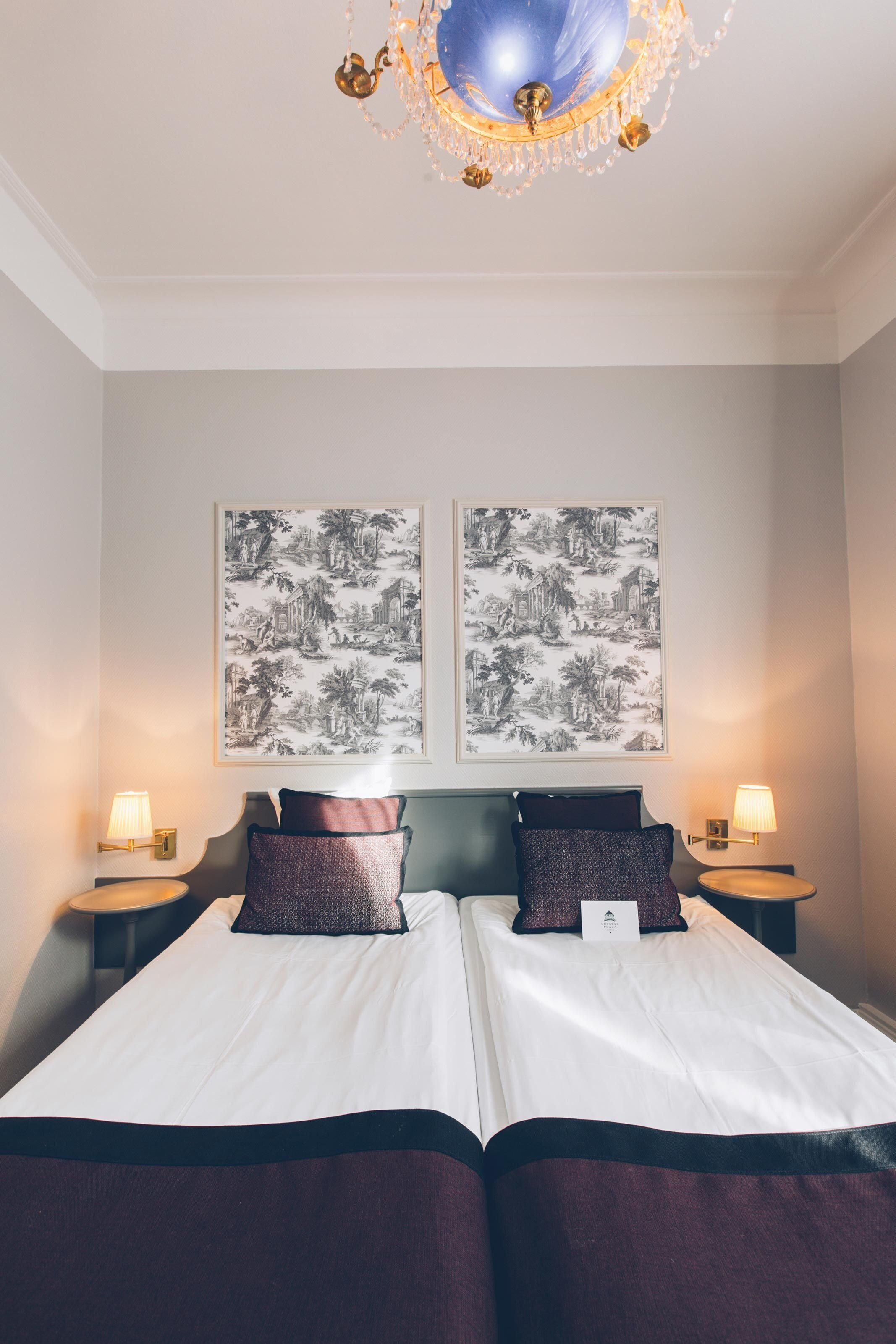 Uma cama de casal com cabeceira e peseira escuras, duas luminárias fixadas na parede e duas pinturas em preto e branco retratando paisagens emolduradas.