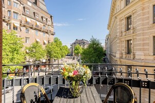 Un balcón con vistas a una calle de la ciudad, un jarrón de flores y una mesa con sillas.