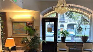 A lobby with a chandelier, a map on the wall, a seating area with a table, and potted plants.