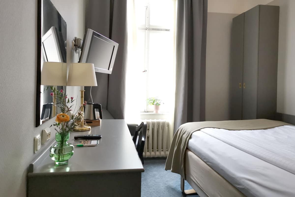 Ett hotellrum med en säng, ett skrivbord med en lampa, en tv och ett fönster med gardiner.