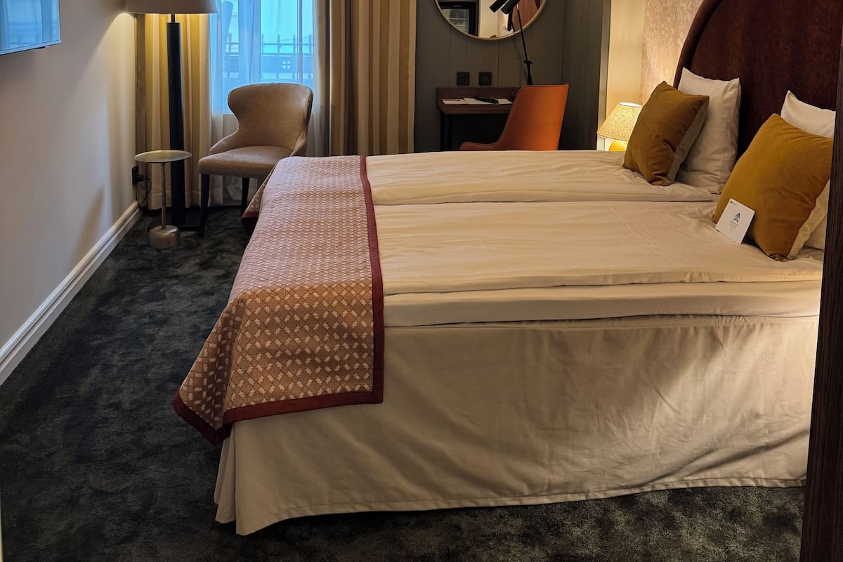 Ett hotellrum med en stor säng, en rund spegel, ett skrivbord och en stol.