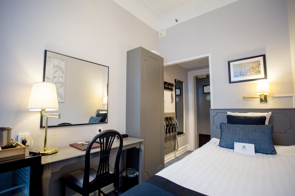 Ett hotellrum med en säng, ett skrivbord, en stol och en spegel.