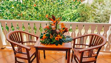Uma mesa de madeira com cadeiras numa varanda com guarda de proteção branca, rodeada por vegetação exuberante.