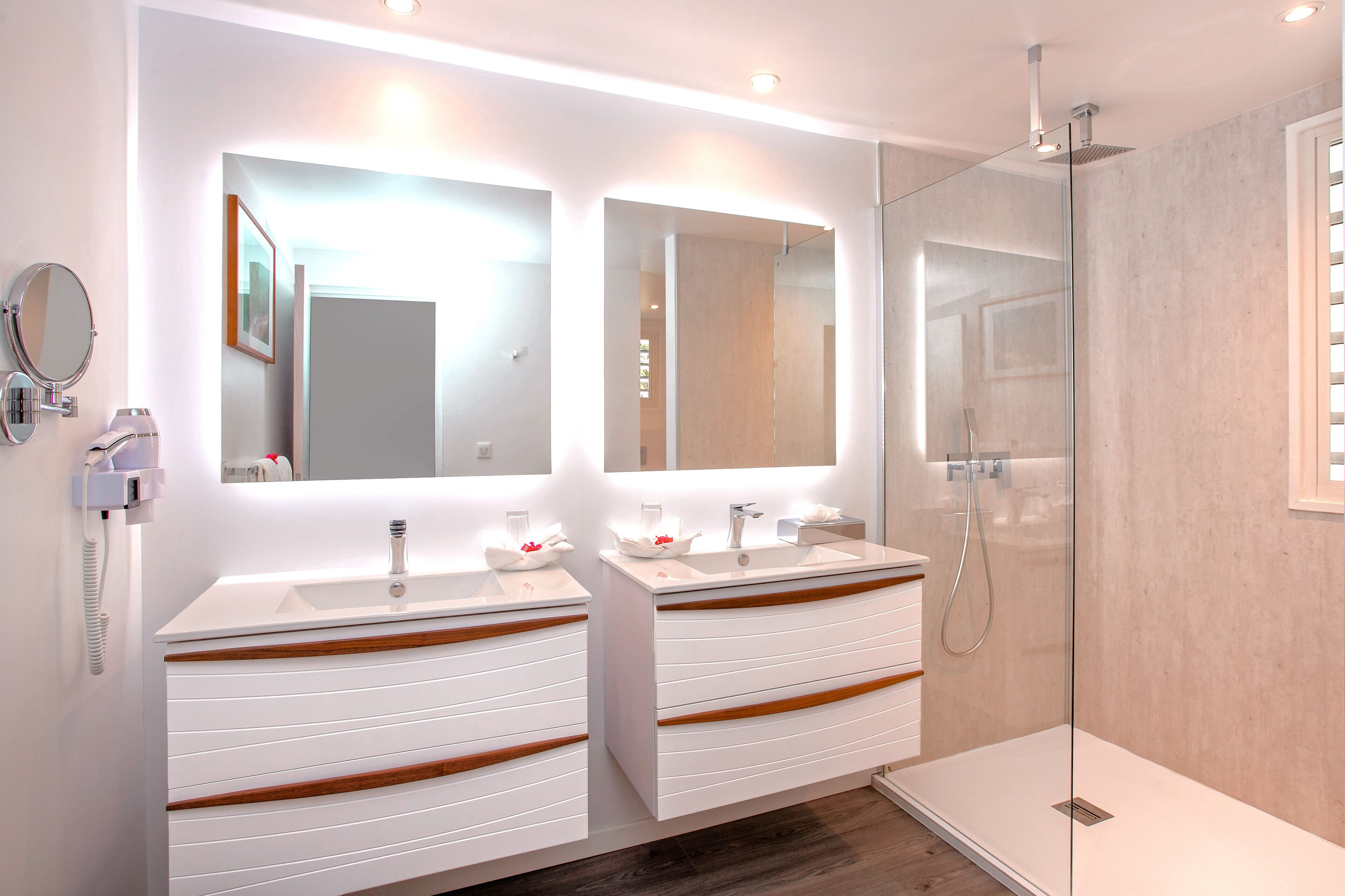Un baño moderno con dos lavamanos, una cabina de ducha con mampara de vidrio y un espejo sobre cada lavamanos.