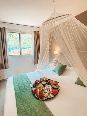 A bed with a canopy, a tray of food, and a window with curtains. - Hotel La Plantation (Orient Bay)
