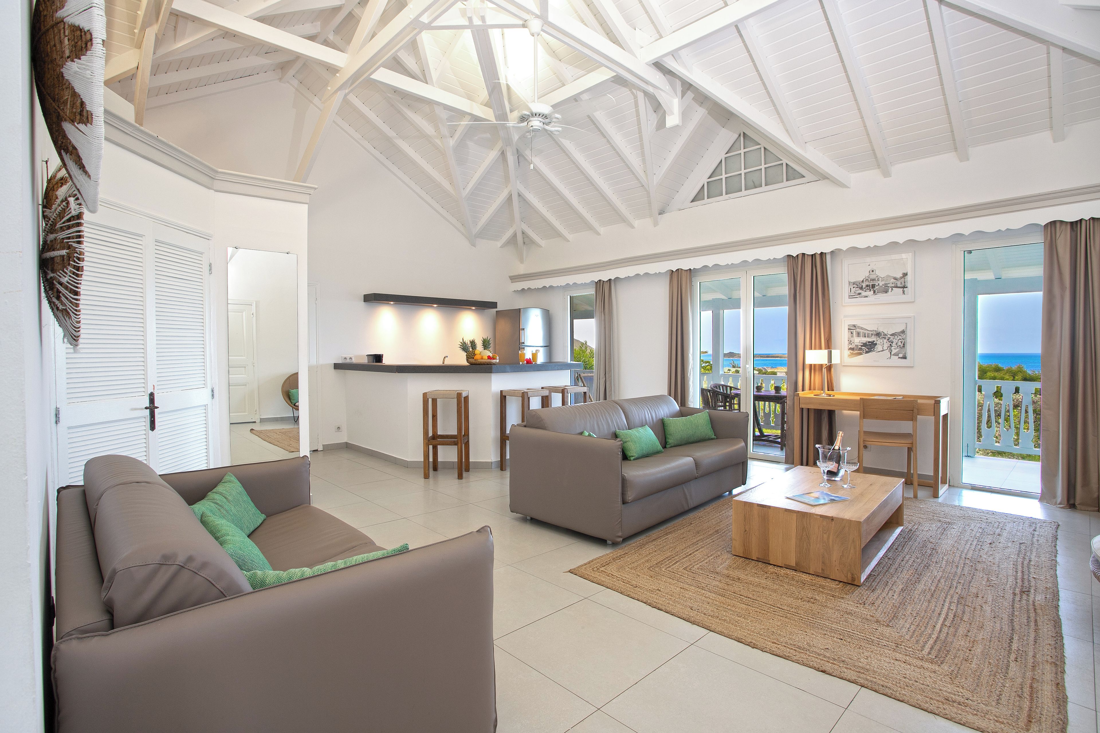 A spacious living area with a high ceiling, a kitchen, and a balcony with a view.