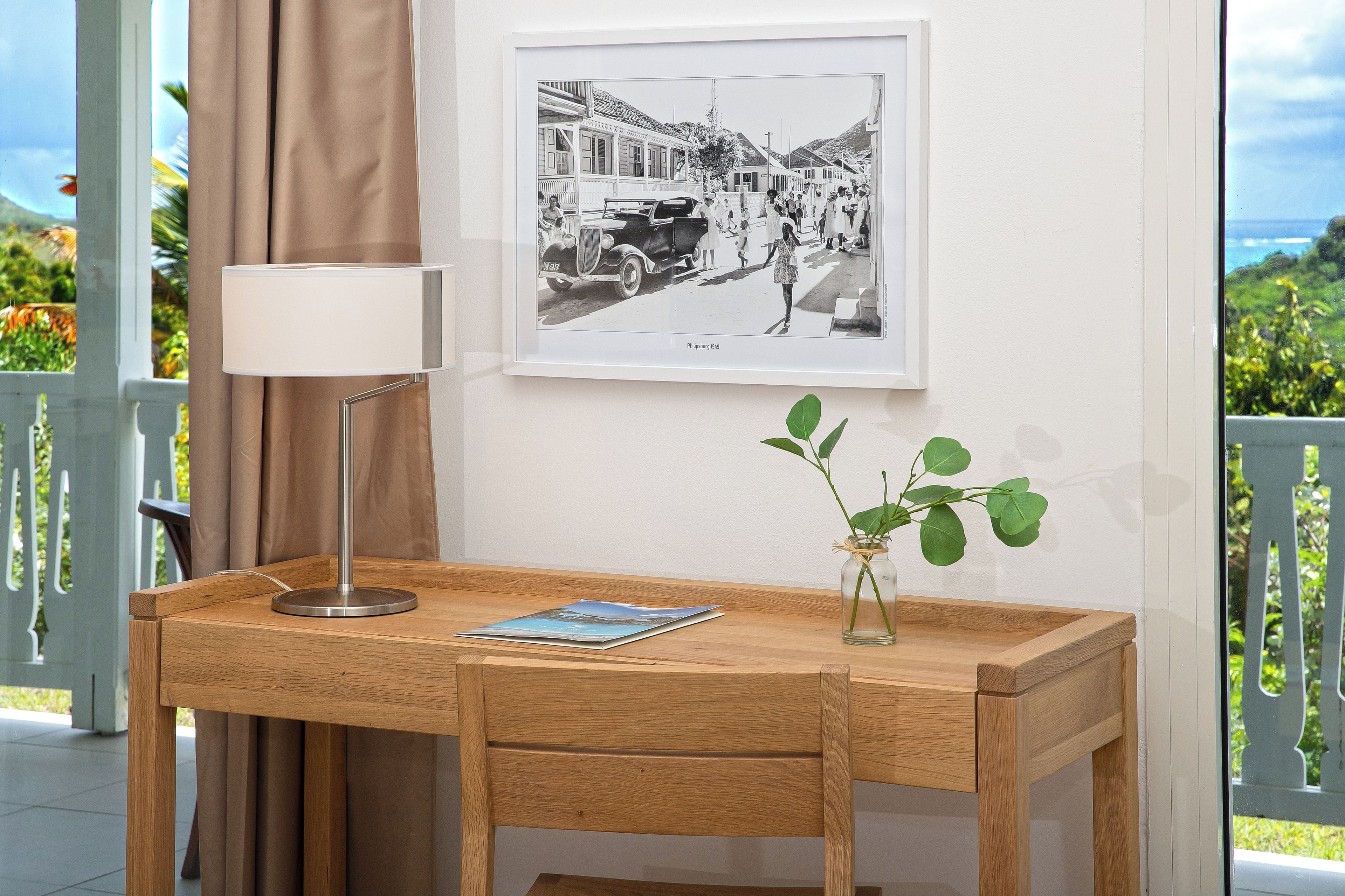 Un bureau en bois, une lampe, une photographie en noir et blanc encadrée et un vase avec une plante.