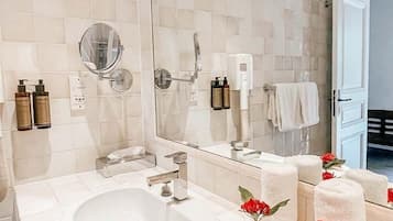 Un baño moderno con un espejo grande, un lavamanos y un inodoro. Hay artículos de aseo en la pared y toallas en el suelo.