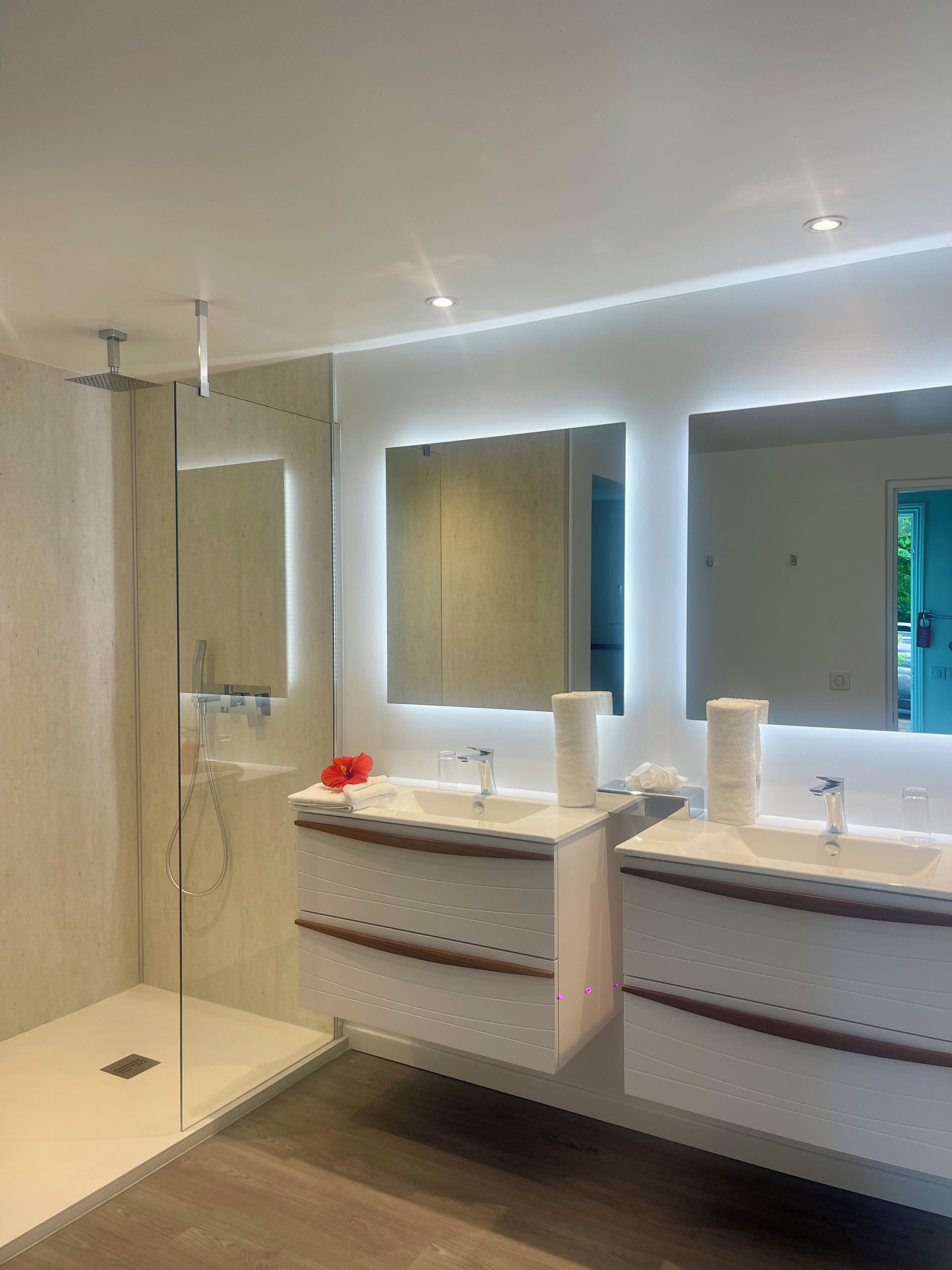Une salle de bain moderne avec deux lavabos, une douche à l’italienne en verre et un grand miroir.