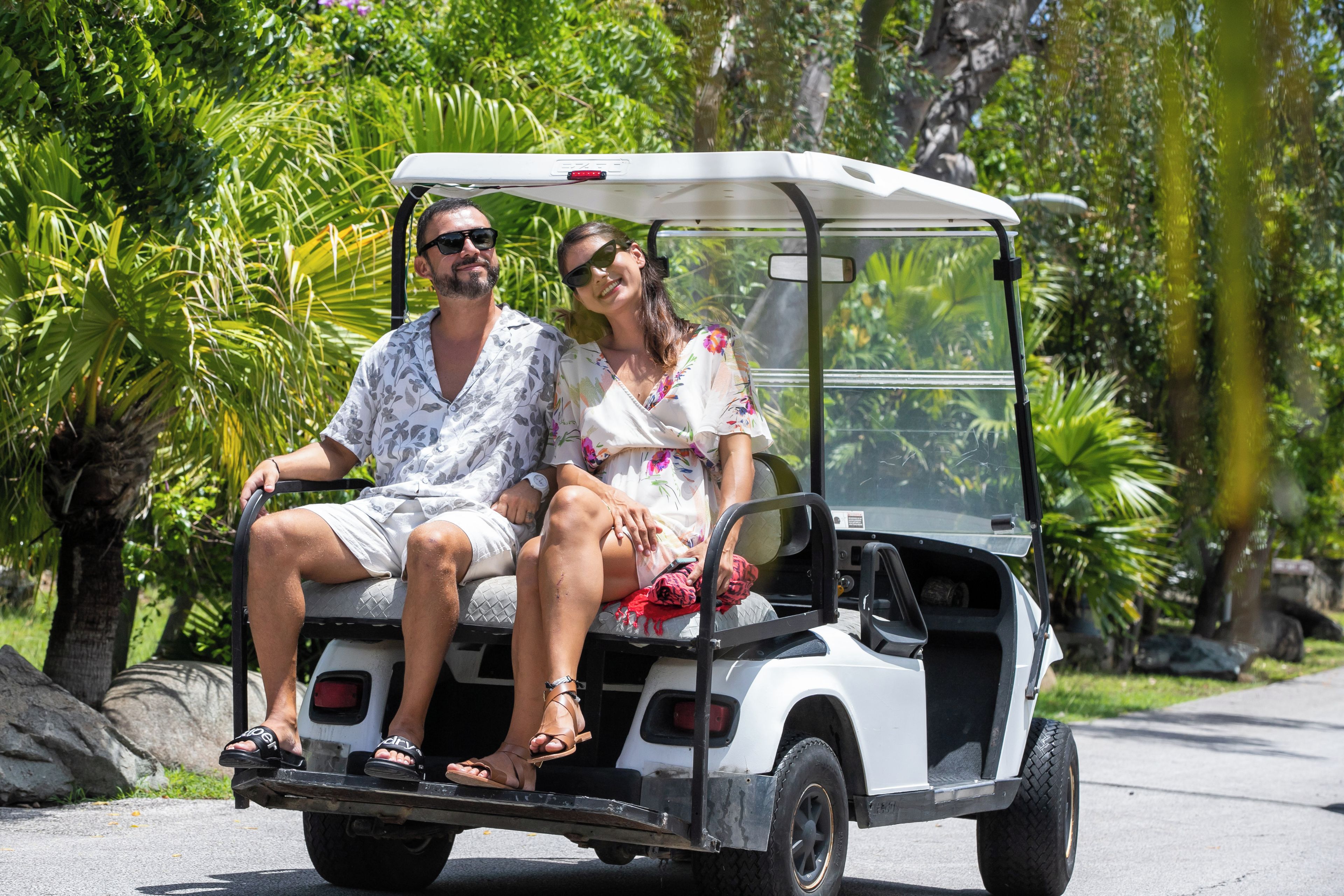 A couple seated in a golf cart with a tropical backdrop.