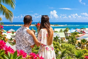 Una pareja contempla una vista costera con playa y edificios coloridos al fondo.