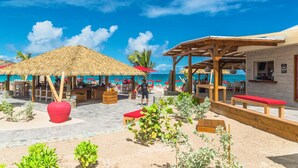 A beachside area with thatched umbrellas, wooden seating, and a bar area. - Hotel La Plantation (Orient Bay)