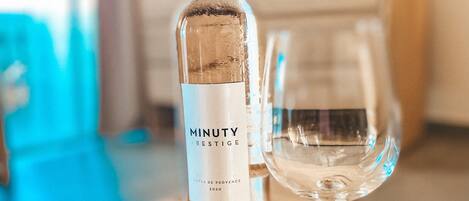 Una botella de vino Minuty Prestige, una copa y una flor roja sobre una mesa de madera.