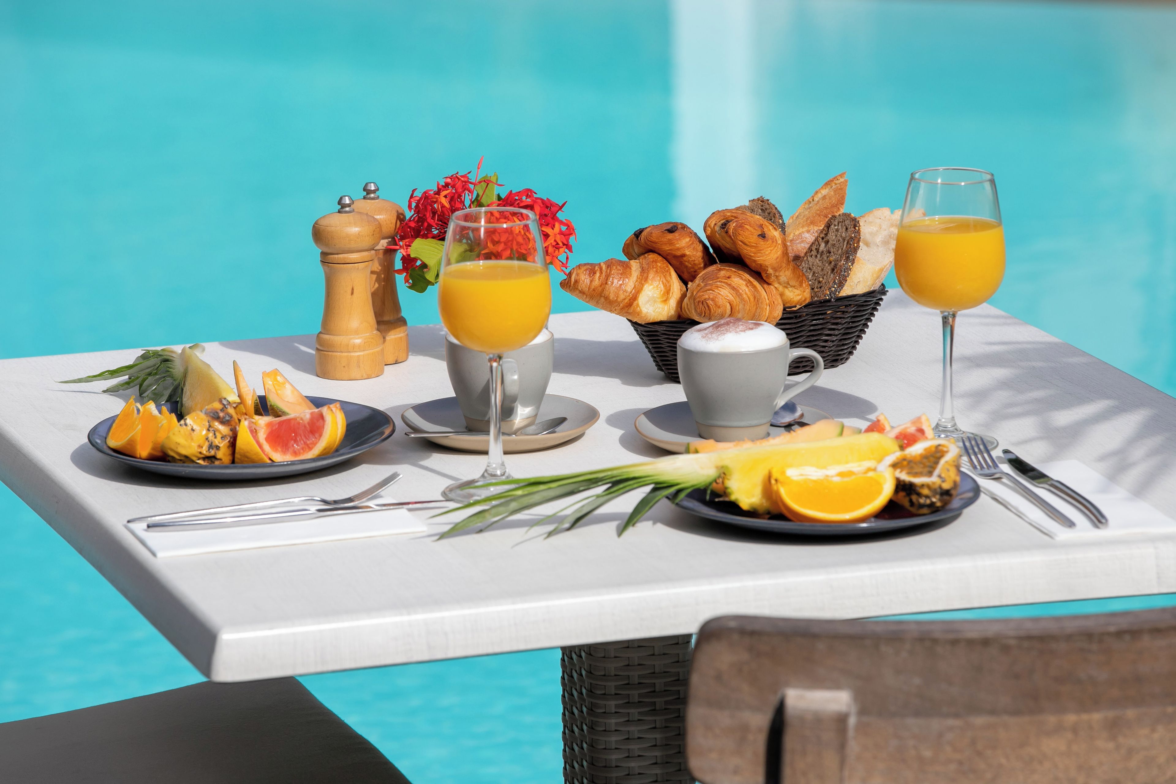 Desayuno junto a una piscina con croissants, zumo de naranja y fruta.