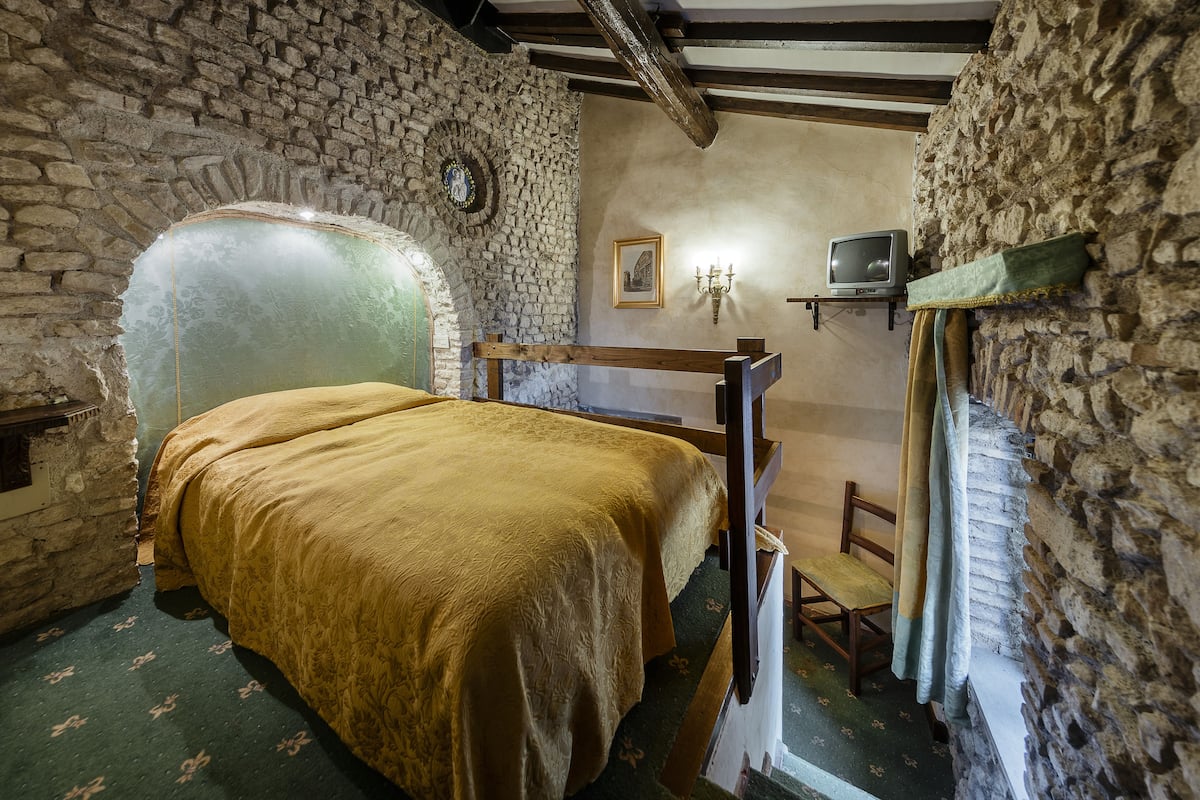 Una habitación con cama, una pequeña televisión y paredes de piedra.