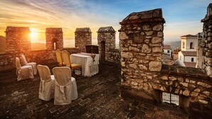 A stone terrace with tables and chairs, overlooking a historic town. - Castello Orsini Hotel (Nerola)