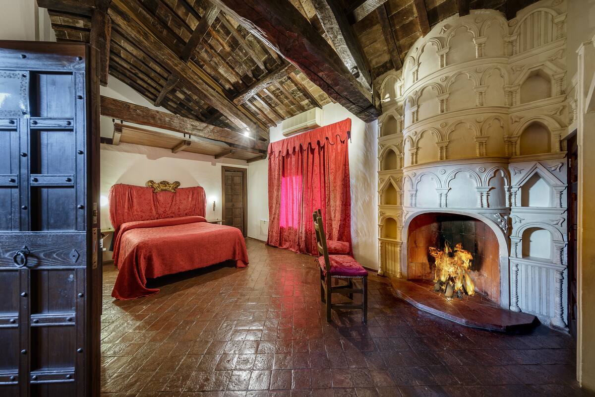 Una habitación con techo de madera, chimenea, cama con ropa de cama roja y una silla.