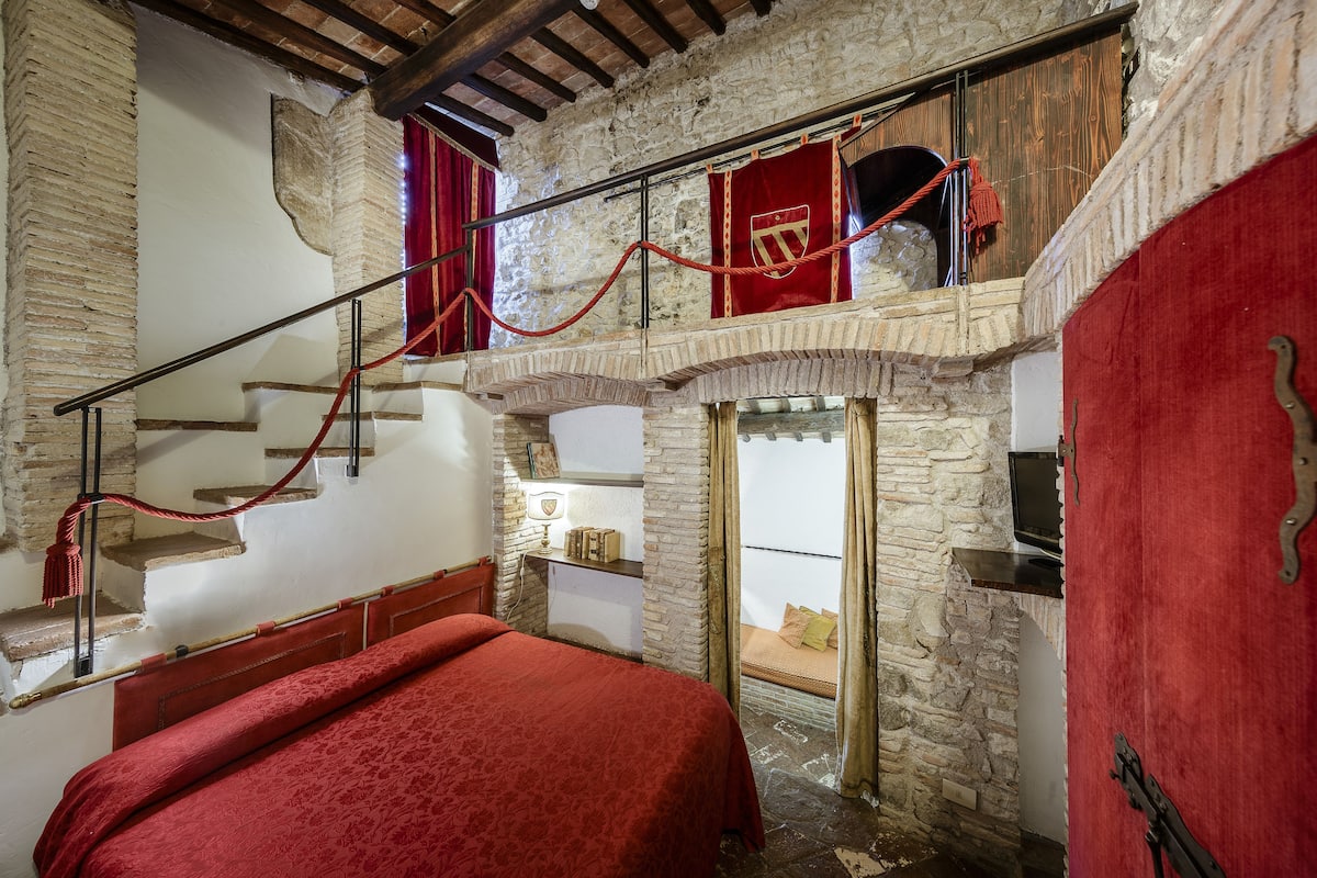 Una habitación con una cama, una escalera y una pared de piedra.