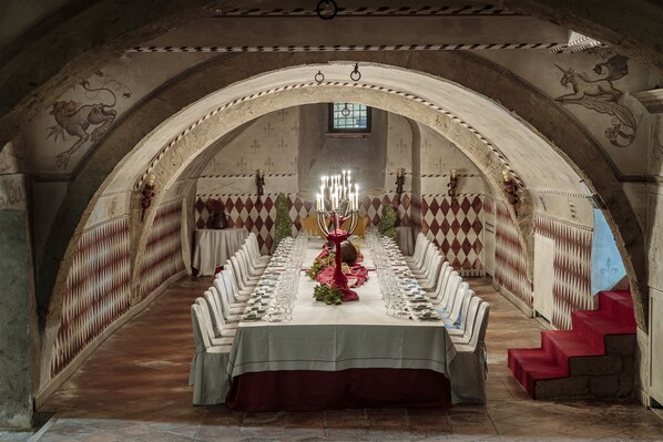 A long banquet table set for a formal event in a historic building with arched ceilings and detailed wall decorations. - Castello Orsini Hotel (Nerola)