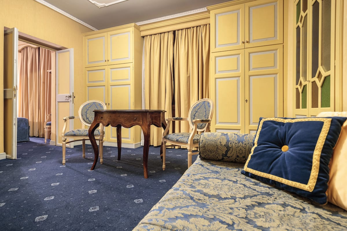 Una habitación con alfombra estampada, un sofá con cojín azul y dorado, y una mesa de madera.