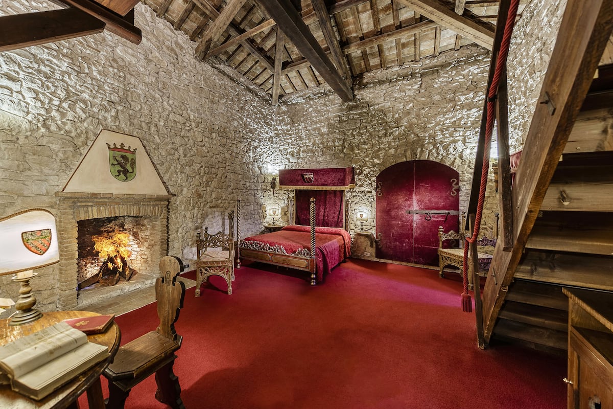 Una habitación de estilo medieval con paredes de piedra, una cama con dosel, una chimenea y una alfombra roja.