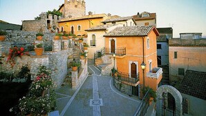 A historic building with a stone facade, a tower, and a courtyard with steps leading to a gate. - Castello Orsini Hotel (Nerola)