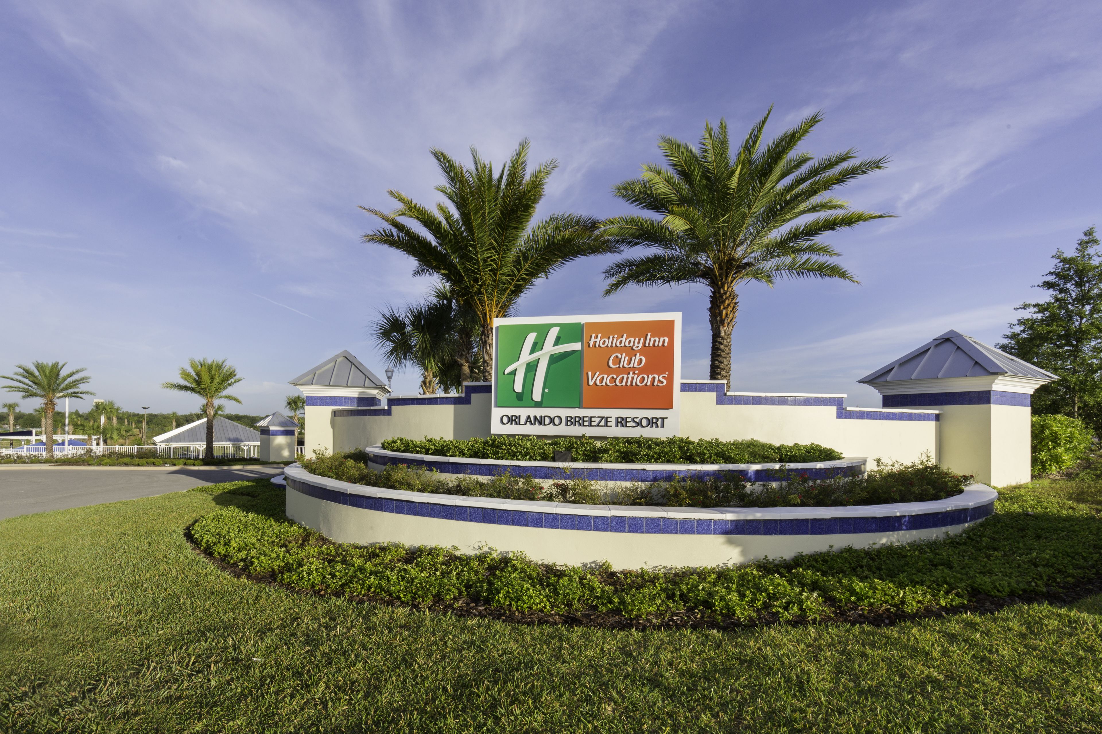 Señal de Holiday Inn Club en Orlando Breeze Resort, con palmeras y un cielo despejado.