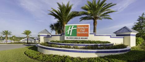 Señal de Holiday Inn Club en Orlando Breeze Resort, con palmeras y un cielo despejado.