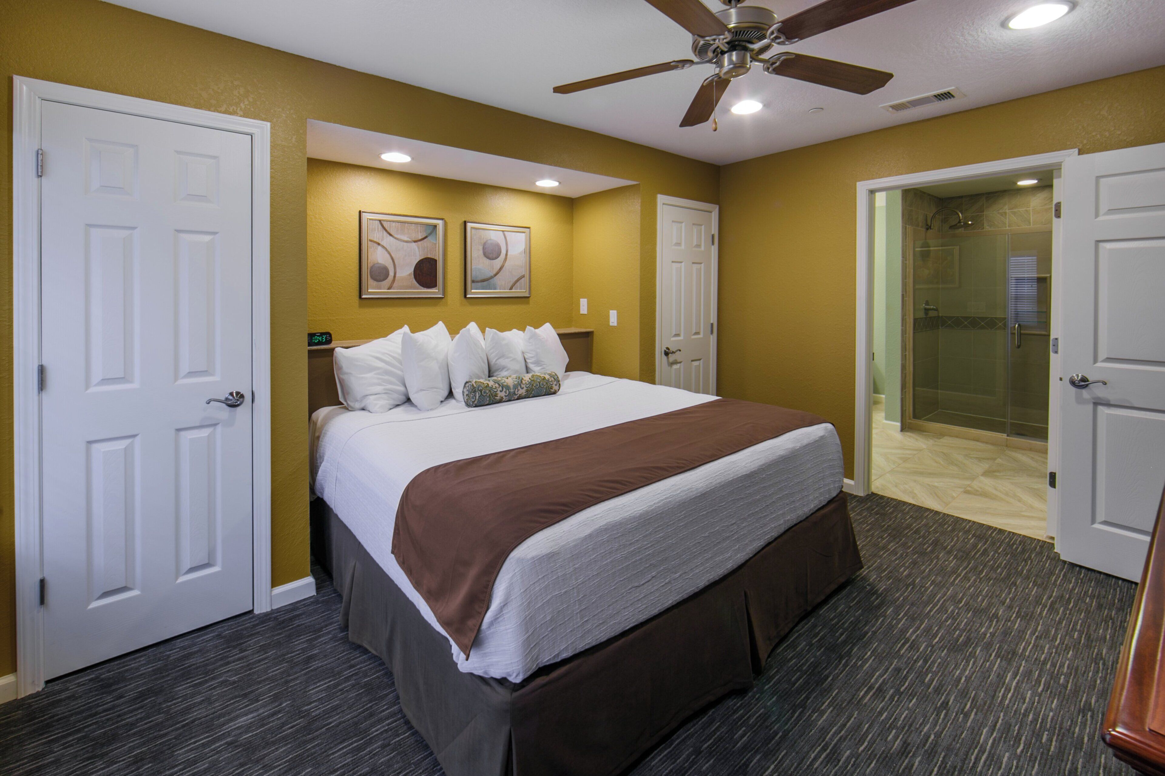 A hotel room with a bed, a ceiling fan, and a shower area.