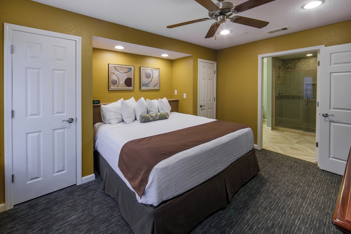 Una habitación de hotel con cama, ventilador de techo y zona de ducha.