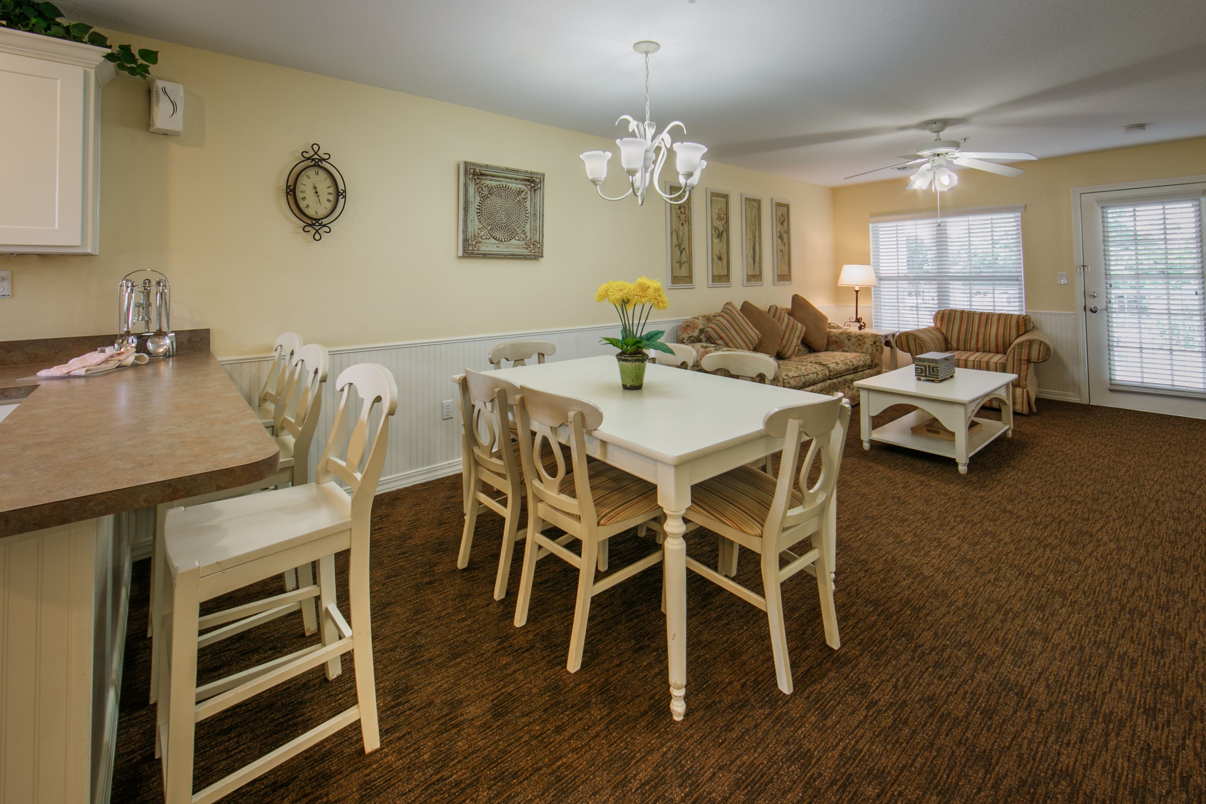 A dining area with a white table and chairs, a chandelier, and a sofa with cushions.