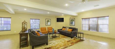 A spacious living room with a gray sofa, orange armchairs, a coffee table, and a ceiling fan.