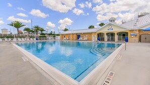 A swimming pool with a lifeguard tower, lounge chairs, and a covered area with a clock.