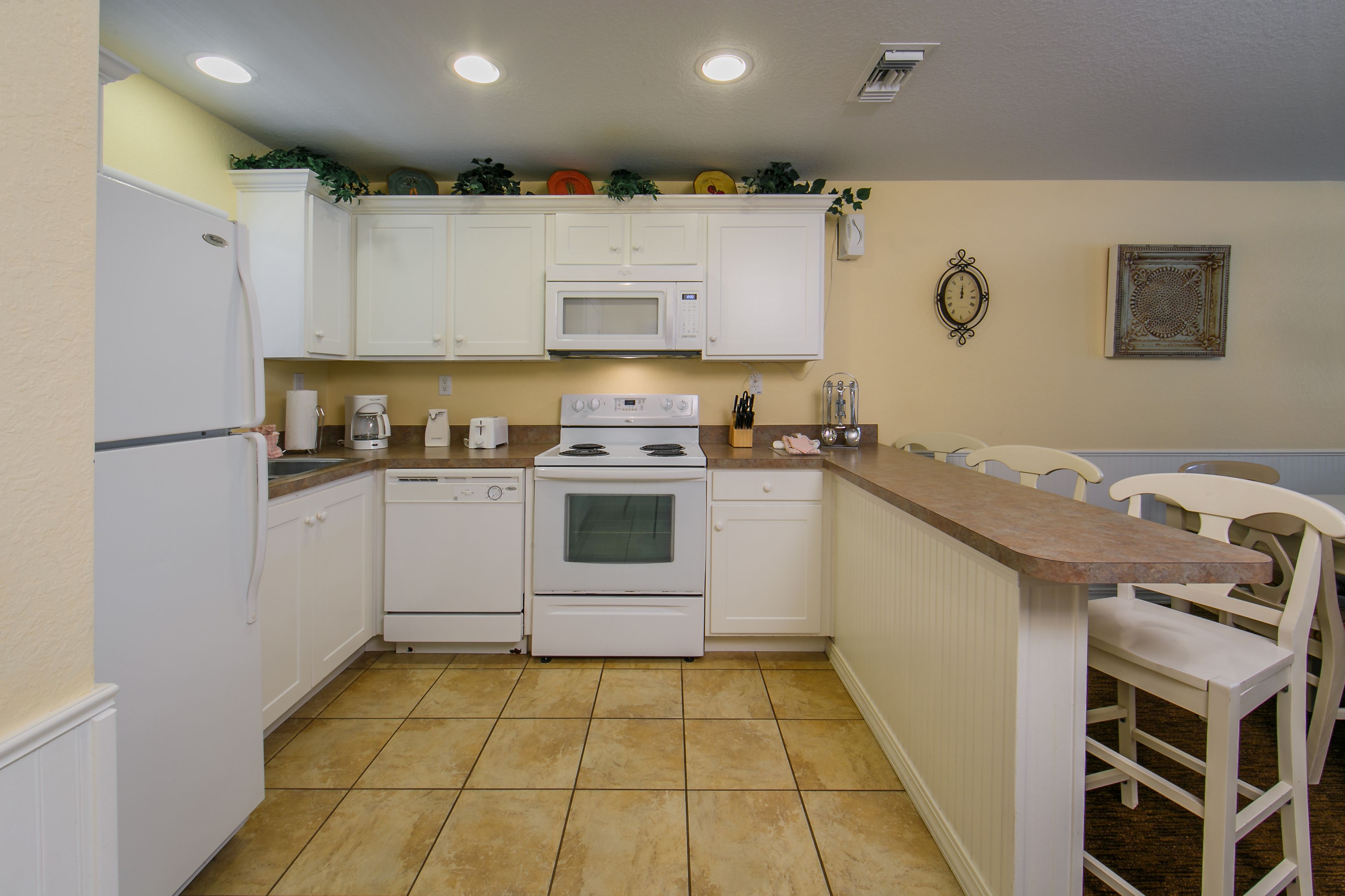 A kitchen with white cabinets, a microwave, an oven, and a sink. There are two chairs and a countertop.