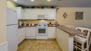 A kitchen with white cabinets, a microwave, an oven, and a sink. There are two chairs and a countertop.