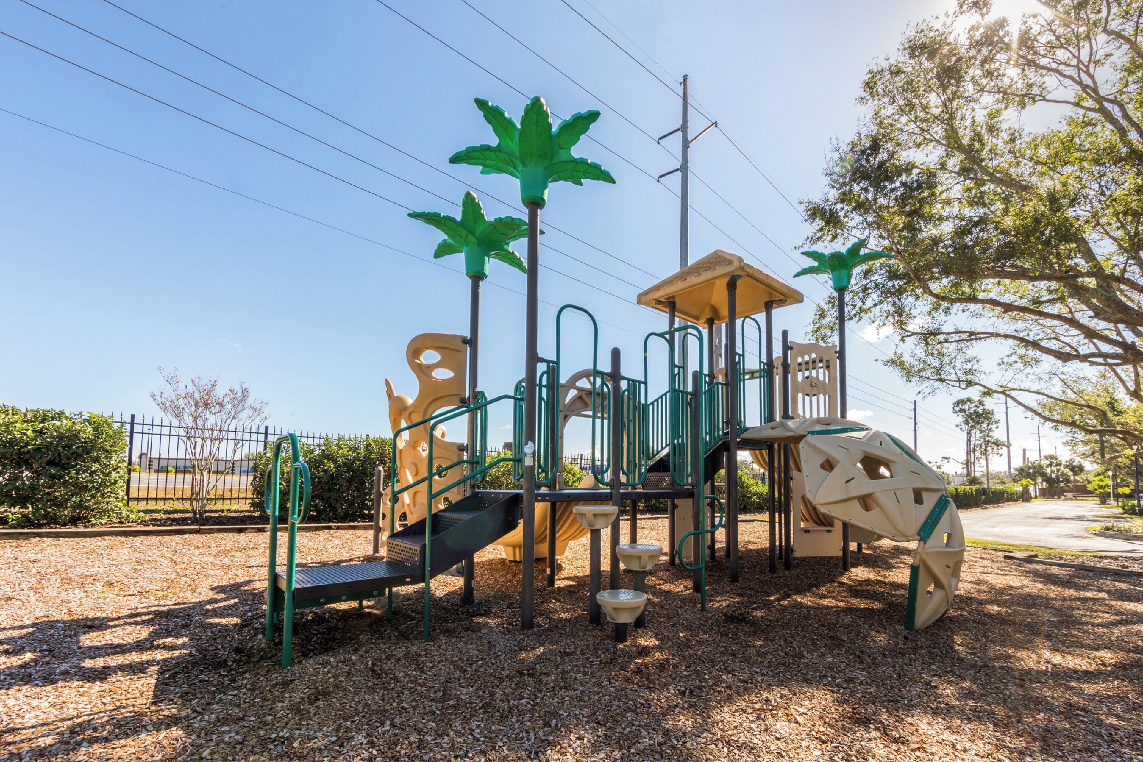 Un parque infantil con estructuras para escalar y toboganes, rodeado por una valla y árboles.
