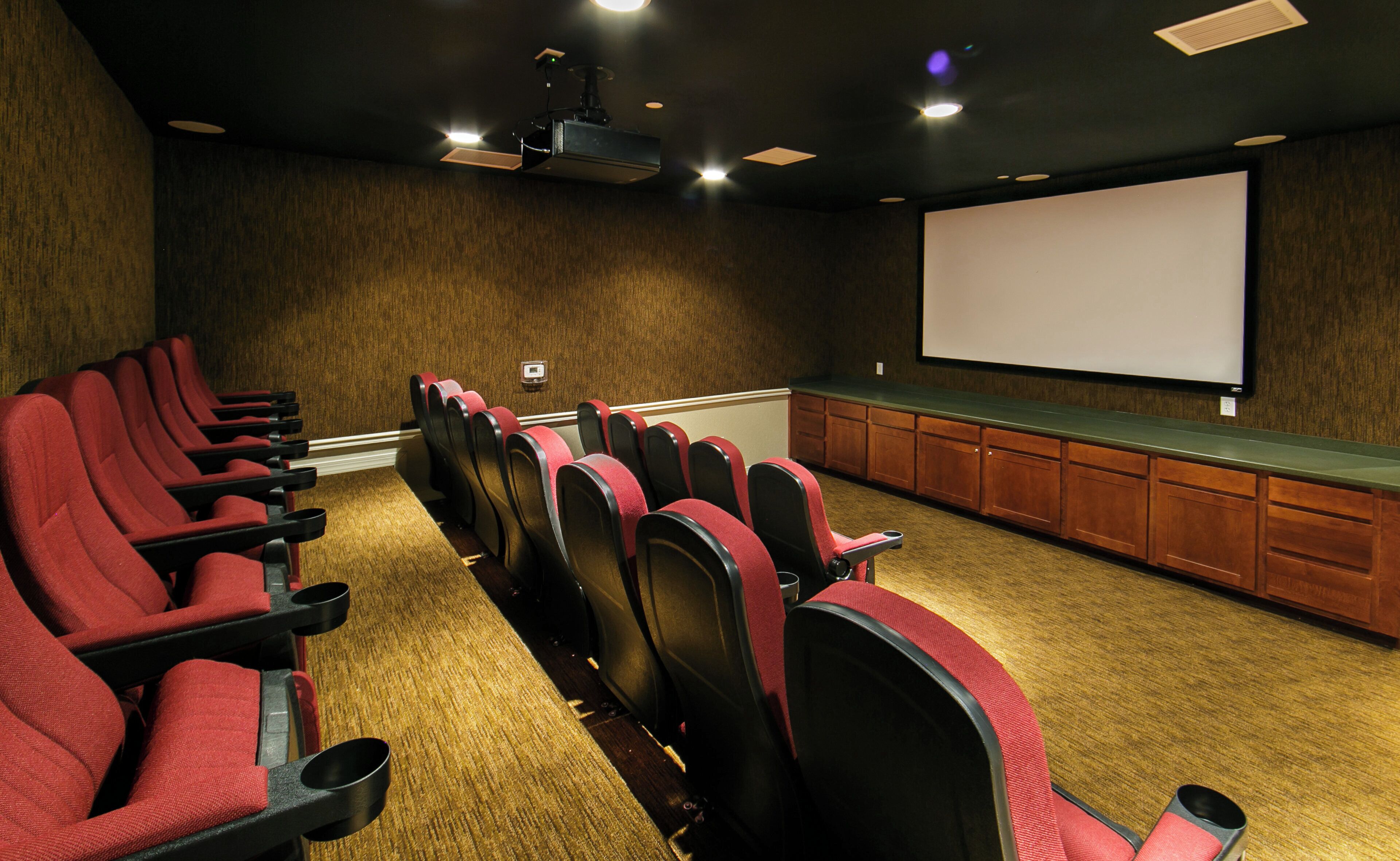 A conference room with rows of red chairs, a projector screen, and a wooden paneling wall.