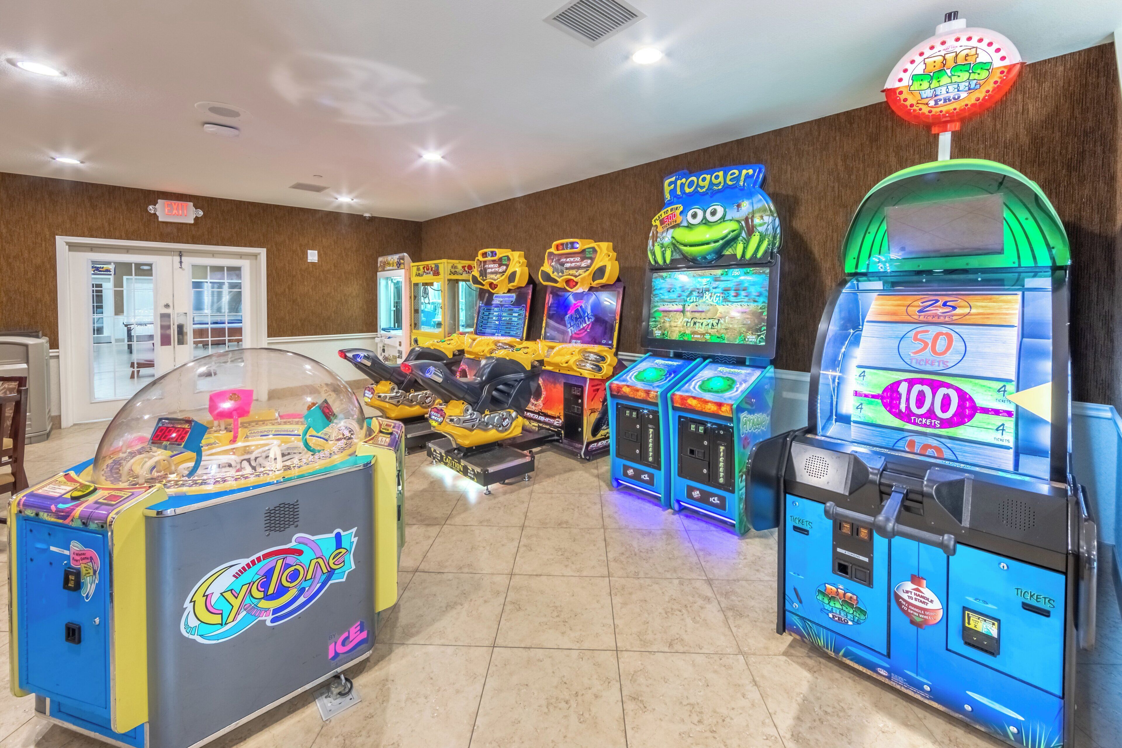 Una hilera de juegos de arcade en una sala con piso de baldosas y paredes de madera.