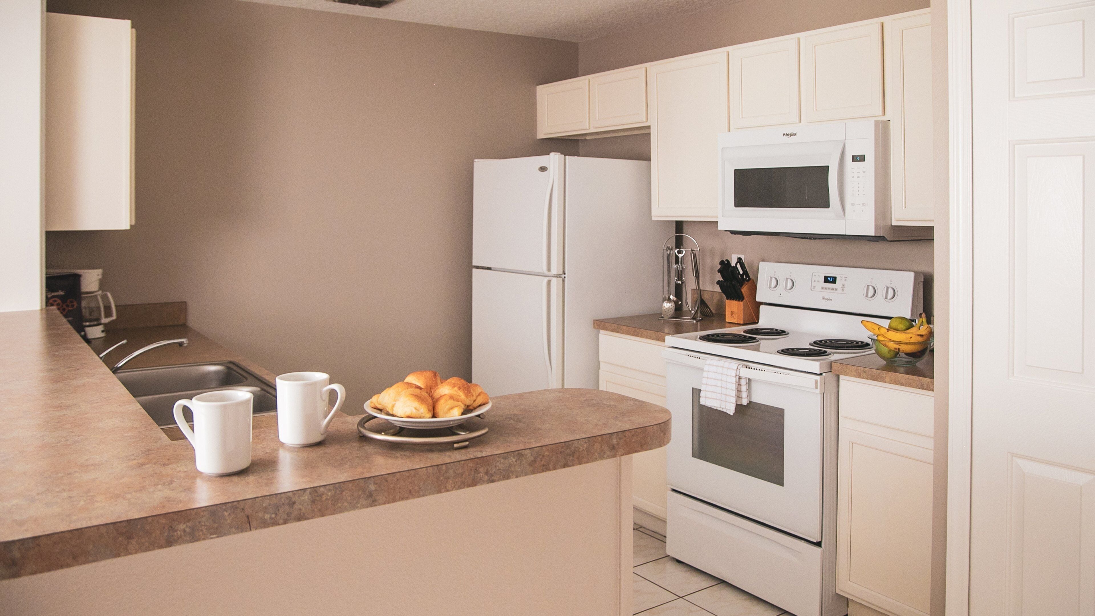 A modern kitchen with white appliances, a sink, and a countertop with croissants and coffee cups.