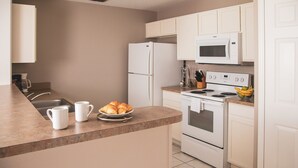 A modern kitchen with white appliances, a sink, and a countertop with croissants and coffee cups. - Holiday Inn Club Vacations Orlando Breeze Resort by IHG (Davenport)